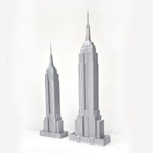 May include: Two silver miniature models of the Empire State Building. The larger model is highly detailed, with a spire and multiple tiers. The smaller model is also detailed, with a similar design. Both models stand on a white surface.