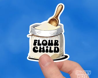 May include: A white flour bag with a brown wooden spoon sticking out of the top. The bag has the text "Flour Child" printed on it in black with a flower design.