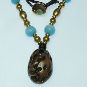 May include: A necklace with a brown wooden pendant, blue glass beads, and gold accents. The necklace is made with black cord and has a sliding knot closure.