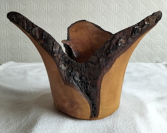May include: A wooden bowl with a natural bark edge. The bowl is made from a single piece of wood and has a unique, organic shape.