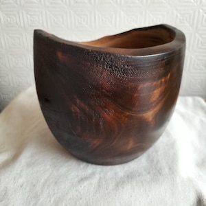 May include: A large, dark brown wooden bowl with a smooth, rounded interior. The bowl is made from a single piece of wood and has a natural, rustic look.