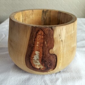 May include: A large wooden bowl with a natural wood finish. The bowl has a unique design with a knot in the wood that has been left exposed and polished.