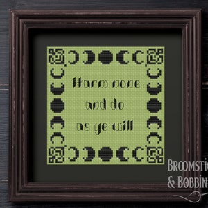 May include: A framed cross-stitch pattern with a green background and black text that reads "Harm none and do as ye will". The text is surrounded by a border of black crescent moons. The frame is brown wood and the text "Harm None" is written in white below the frame.