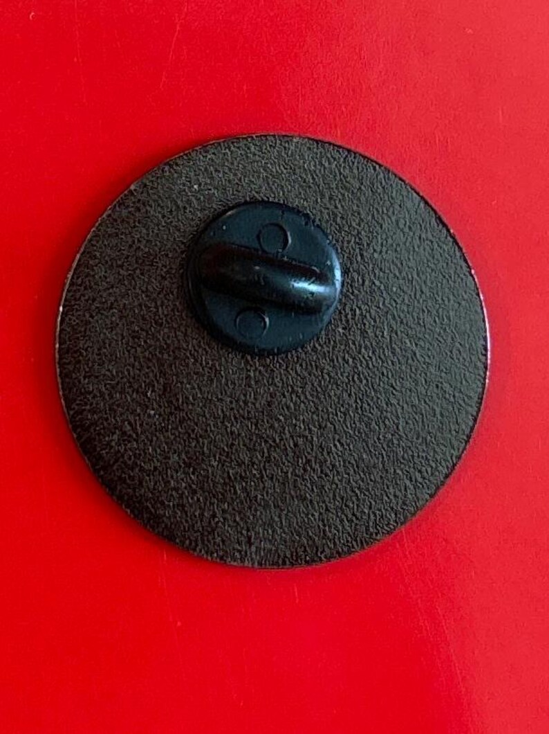 May include: The back of a round, black pin with a metal pin back.