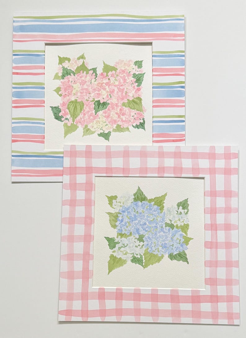May include: Two square watercolor paintings featuring floral arrangements. The top painting shows pink hydrangea blossoms with green leaves, framed by a border of horizontal blue, pink, and green stripes. The bottom painting displays blue and white hydrangea flowers with green leaves, set within a pink and white checkered border.