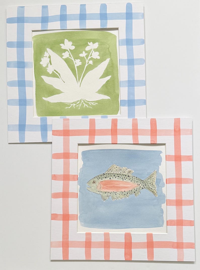 May include: Two square art prints with white borders featuring a blue and white gingham pattern on one and a coral and white gingham pattern on the other. The first print shows a white botanical illustration on a green background, while the second print displays a speckled fish with a pink stripe on a light blue background.