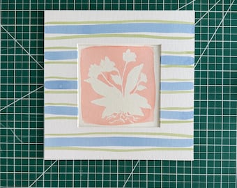 May include: A square art print featuring a central peach-colored square with a white silhouette of a flowering plant. The surrounding mat board displays horizontal light blue and pale green stripes. The print measures 6 inches by 6 inches.