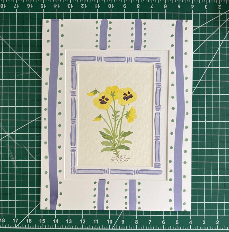 Puede incluir: Una l&aacute;mina rectangular con una ilustraci&oacute;n en acuarela de pensamientos amarillos con tallos y ra&iacute;ces verdes. La obra est&aacute; enmarcada por un borde de color violeta claro estilo bamb&uacute; y un paspart&uacute; blanco con rayas verticales.