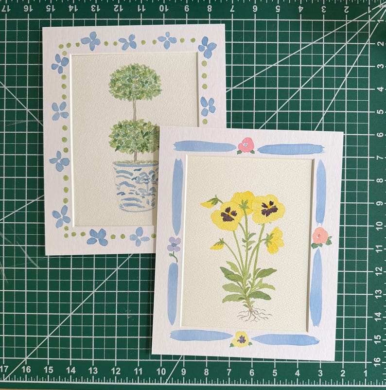 Puede incluir: Dos l&aacute;minas rectangulares sobre papel blanco. Una muestra un topiario verde de dos bolas en una maceta azul y blanca, enmarcado por flores azules y puntos verdes. La otra presenta pensamientos amarillos con tallos y ra&iacute;ces de color verde.