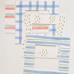 May include: A set of four square paper picture mats featuring hand-painted patterns. The designs include horizontal stripes in coral, light blue, and lime green, a light blue grid pattern, and vertical lime green brushstroke dashes on white.