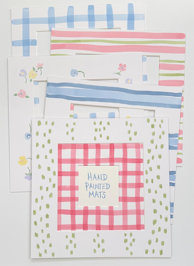 May include: A collection of five rectangular paper picture mats featuring various hand-painted designs including blue plaid, pink and green stripes, small floral patterns, blue horizontal stripes, and a red plaid border with the text HAND PAINTED MATS.