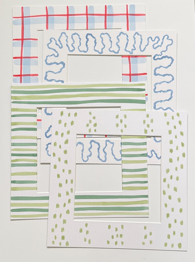 May include: A set of four square paper picture mats featuring hand-painted designs. The patterns include a blue and red plaid, a light blue wavy line, horizontal green stripes, and light green vertical dashes on a white background.