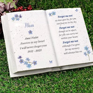 May include: A white book-shaped memorial with a forget-me-not flower design and the text "Nan Anni Violet Forever in my heart I will never forget you 1952-2023 Forget me not as time goes by, for you can find me in the sky. Forget me not though we're apart, for you can carry me within your heart. Forget me not although I've gone for my memory will always live on."
