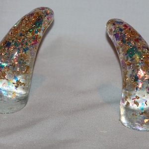 May include: Two clear glass horns with gold and iridescent glitter embedded inside. The horns are curved and have a pointed tip.