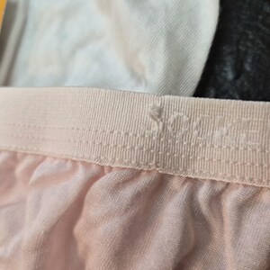 May include: Close-up of light pink underwear. The elasticated waistband is a lighter shade of pink and features the brand name. The fabric of the underwear is soft and slightly creased.