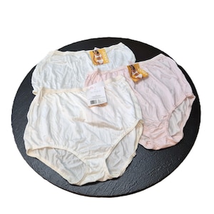 May include: Three pairs of high-waisted underwear in white and pink shades, presented on a black circular surface. Each pair has a tag attached. The underwear appears to be made of a soft, possibly silky material.