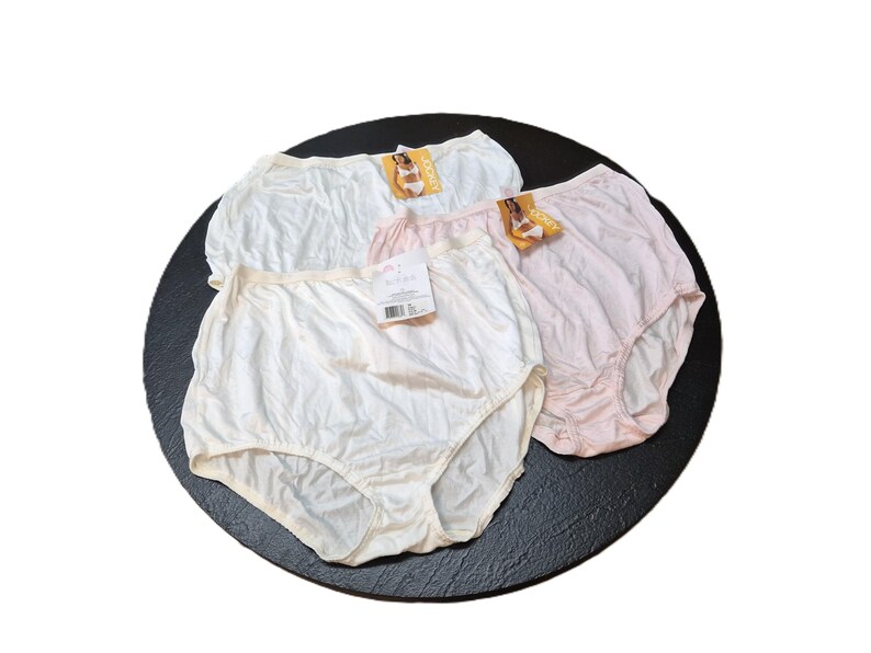 May include: Three pairs of high-waisted underwear in white and pink shades, presented on a black circular surface. Each pair has a tag attached. The underwear appears to be made of a soft, possibly silky material.