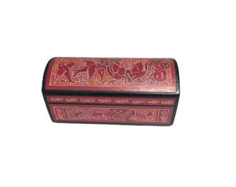 May include: A rectangular, red wooden box with a black trim. The box is adorned with carved, light-colored bird and animal designs. The lid is curved, and the box appears to be closed. The box is likely used for storage.