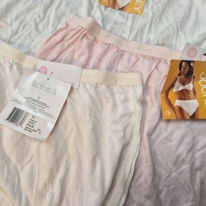 May include: Close-up of several pairs of Jockey underwear in white and light pink. Each pair has a tag attached. The tags feature a picture of a woman wearing Jockey underwear and the Jockey logo.
