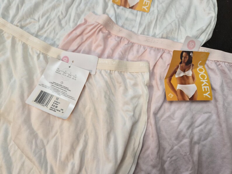 May include: Close-up of several pairs of Jockey underwear in white and light pink. Each pair has a tag attached. The tags feature a picture of a woman wearing Jockey underwear and the Jockey logo.