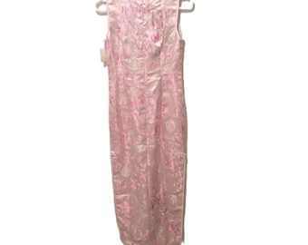 May include: A sleeveless, light pink cheongsam dress featuring a mandarin collar and a repeating floral and circular pattern in a darker shade of pink. The garment is displayed on a white plastic hanger and includes a small white tag on the side.