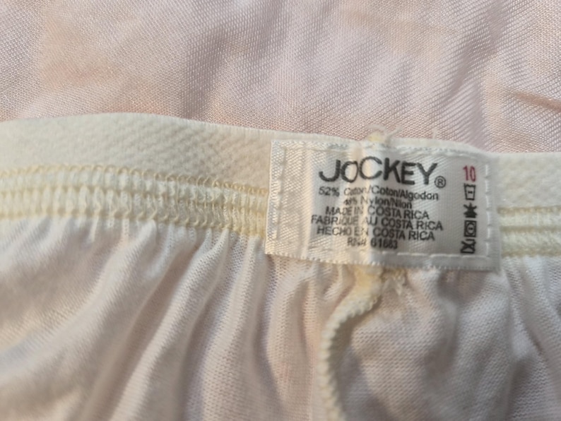 May include: Close-up of white Jockey underwear with a cream elastic waistband. The label reads "JOCKEY", fabric composition, size 10, and "MADE IN COSTA RICA".