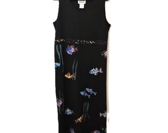 May include: Black sleeveless dress with a scoop neckline, adorned with colorful fish and seaweed patterns. The dress is hanging on a black hanger. The fish are in shades of blue, yellow, and purple.