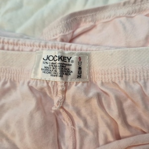 May include: Close-up of light pink Jockey underwear. The tag reads "JOCKEY" and includes the size 9. The fabric is a blend of cotton and nylon. The underwear is made in Costa Rica.