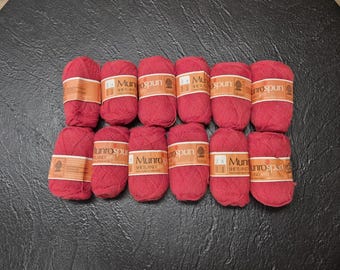 May include: A collection of red yarn skeins, each with a paper label, arranged on a dark surface. The yarn appears soft and fluffy, ideal for knitting or crocheting projects. The labels feature text.