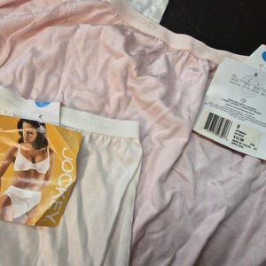 May include: Close-up of three pairs of Jockey underwear in white and pale pink. Each pair has a white waistband and a tag attached. One tag features a woman in a bra and underwear. The other tags have product information.