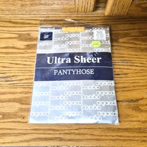 May include: A package of Ultra Sheer pantyhose. The packaging is silver with the word "agaca" printed repeatedly. The words "Ultra Sheer PANTYHOSE" are printed in a dark blue rectangle. A yellow price tag is visible.