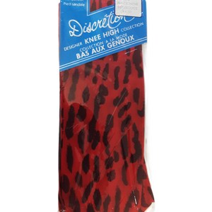 May include: Red and black leopard print knee-high stockings in a clear plastic package. The package has a blue and white label with the text "Discretion" and "Designer Knee High Collection". The stockings are visible through the packaging.