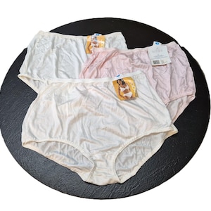 May include: Three pairs of high-waisted underwear in white and pink. Each pair has a tag attached. The underwear is made of a smooth, possibly satin-like material. The items are arranged on a dark, circular surface.