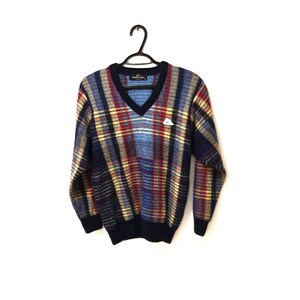 May include: A vintage V-neck sweater with a plaid design in shades of blue, red, and yellow. The sweater features a navy blue collar, cuffs, and hem. A small white logo is on the chest. It is displayed on a black hanger.