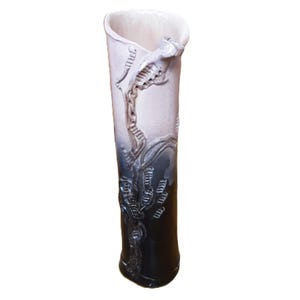 May include: A tall, ceramic vase with a unique design. The vase transitions from a light beige at the top to a deep black at the base. A detailed, raised pattern in a darker gray color adorns the vase, adding texture and visual interest.
