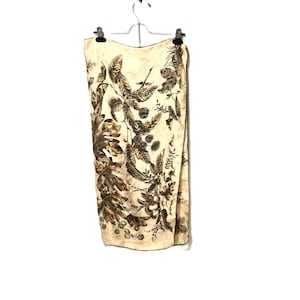 May include: A cream-coloured scarf with a botanical print of leaves and berries in shades of brown and tan. The scarf is hanging on a metal hanger against a white background. The scarf is rectangular in shape.