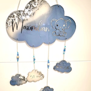 Könnte beinhalten: Wolkenförmige Kinderzimmerdekoration mit dem Namen "Maximilian" in silberner Schrift. Sie zeigt ein blaues Elefanten-Design und hängende Wolkenanhänger mit Geburtsdetails. Die Hauptwolke ist blau und weiß mit silbernen Akzenten.