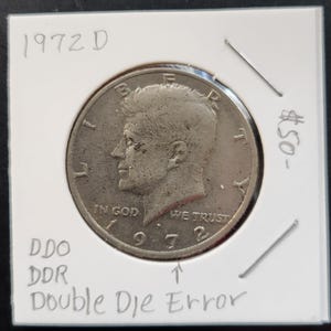 May include: A silver 1972-D John F. Kennedy half dollar coin with a double die error. The coin is in a plastic display case with a white background. The text "DDO DDR Double Die Error" is written on the case.