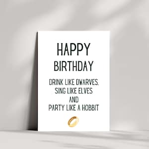 May include: White card with green text that reads "Happy Birthday, Drink like dwarves, sing like elves and party like a hobbit". A gold ring is below the text.