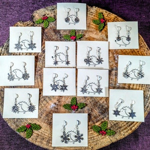 May include: A set of 10 pairs of silver snowflake earrings displayed on a wooden board with red berries and green leaves. Each pair of earrings features a snowflake design with a small hedgehog in the centre.