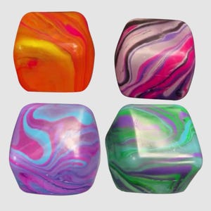 May include: Four colorful, cube-shaped objects with rounded edges. Each cube features a unique swirling pattern of vibrant colors: orange and yellow, pink and purple, blue and pink, and green and purple. The objects have a glossy finish.