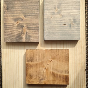 May include: Three wood samples stained in different colors. The first sample is a dark brown, the second is a light gray, and the third is a medium brown.