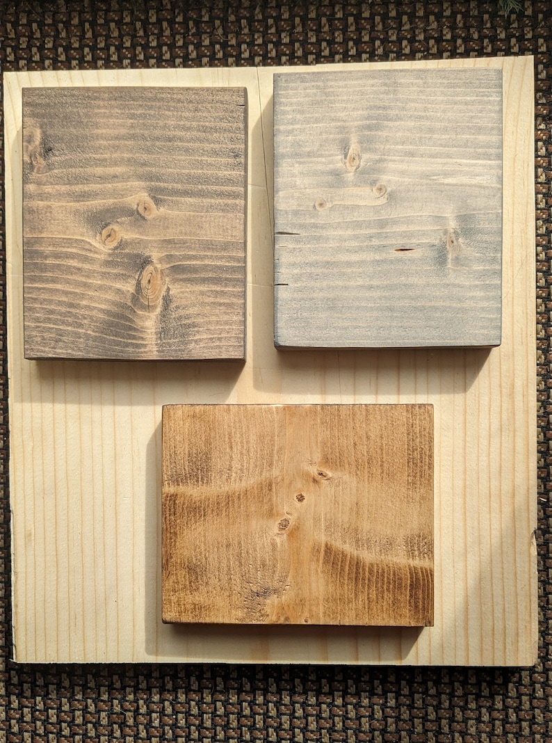 May include: Three wood samples stained in different colors. The first sample is a dark brown, the second is a light gray, and the third is a medium brown.