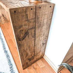 May include: A wooden console table with a distressed brown finish. The table has two shelves and is made of reclaimed wood. A decorative candle holder sits on the top shelf.