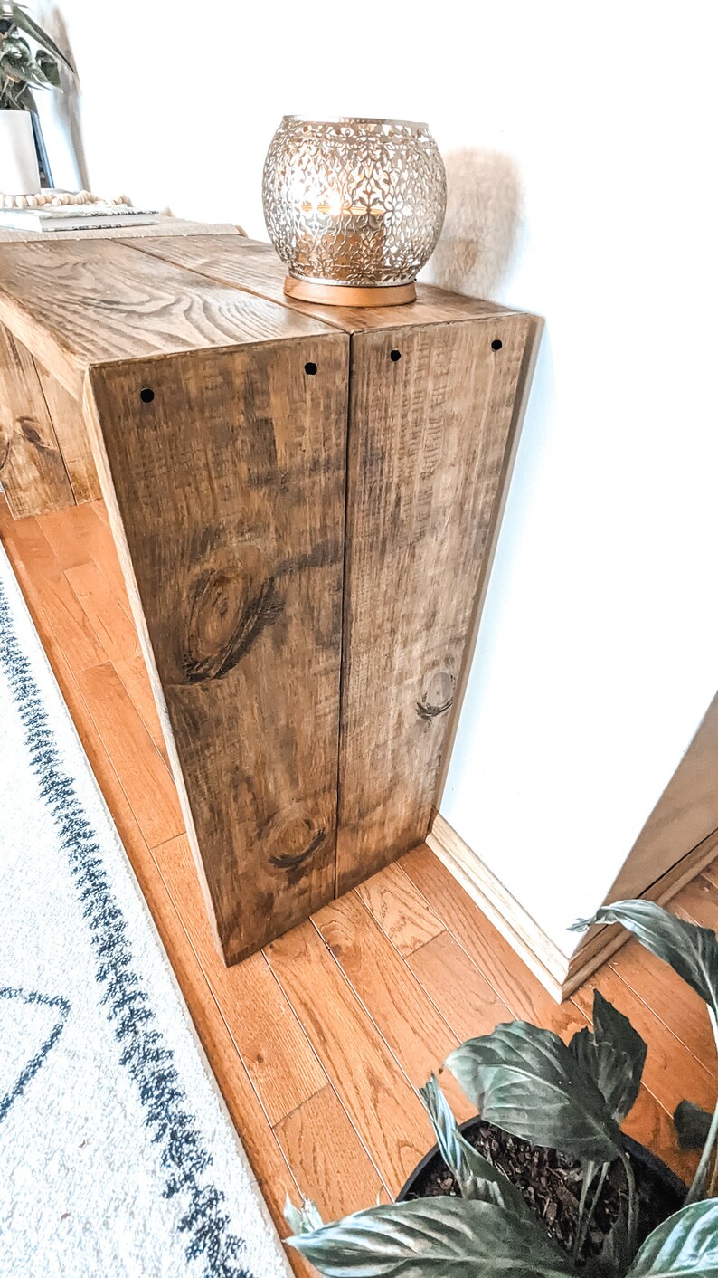 May include: A wooden console table with a distressed brown finish. The table has two shelves and is made of reclaimed wood. A decorative candle holder sits on the top shelf.