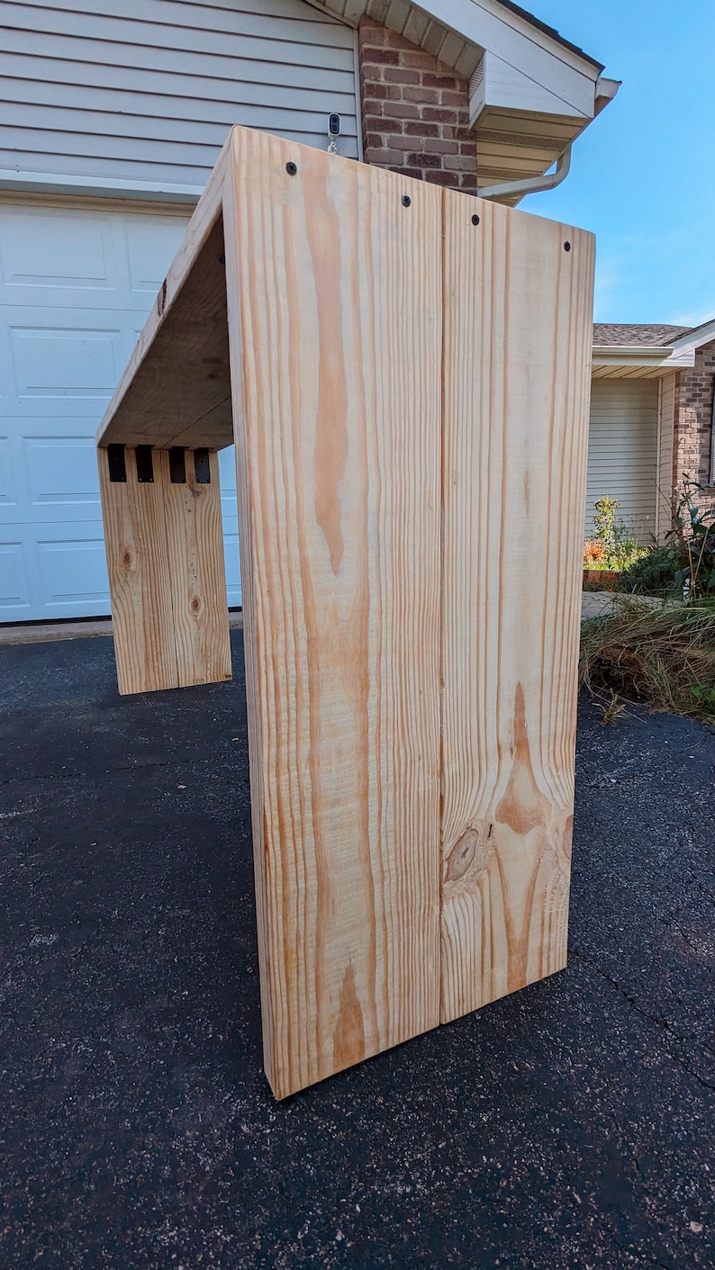 May include: A light wood table with a simple design. The table is made of natural wood and has a light brown finish. The table is shown from the side, with the legs visible. The table is sitting on a black surface.