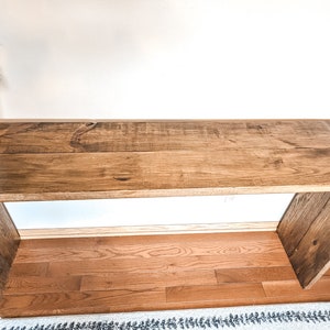 May include: A rustic wooden console table with a natural wood finish. The table has a rectangular top and two open shelves. The table is made of reclaimed wood and has a distressed look.