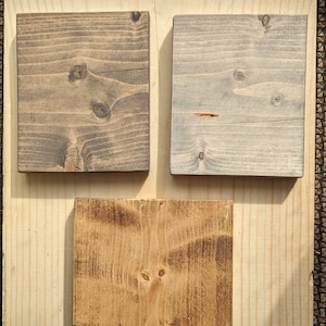 May include: Three wood samples stained in different colors. The first sample is a dark brown color, the second sample is a light gray color, and the third sample is a medium brown color.