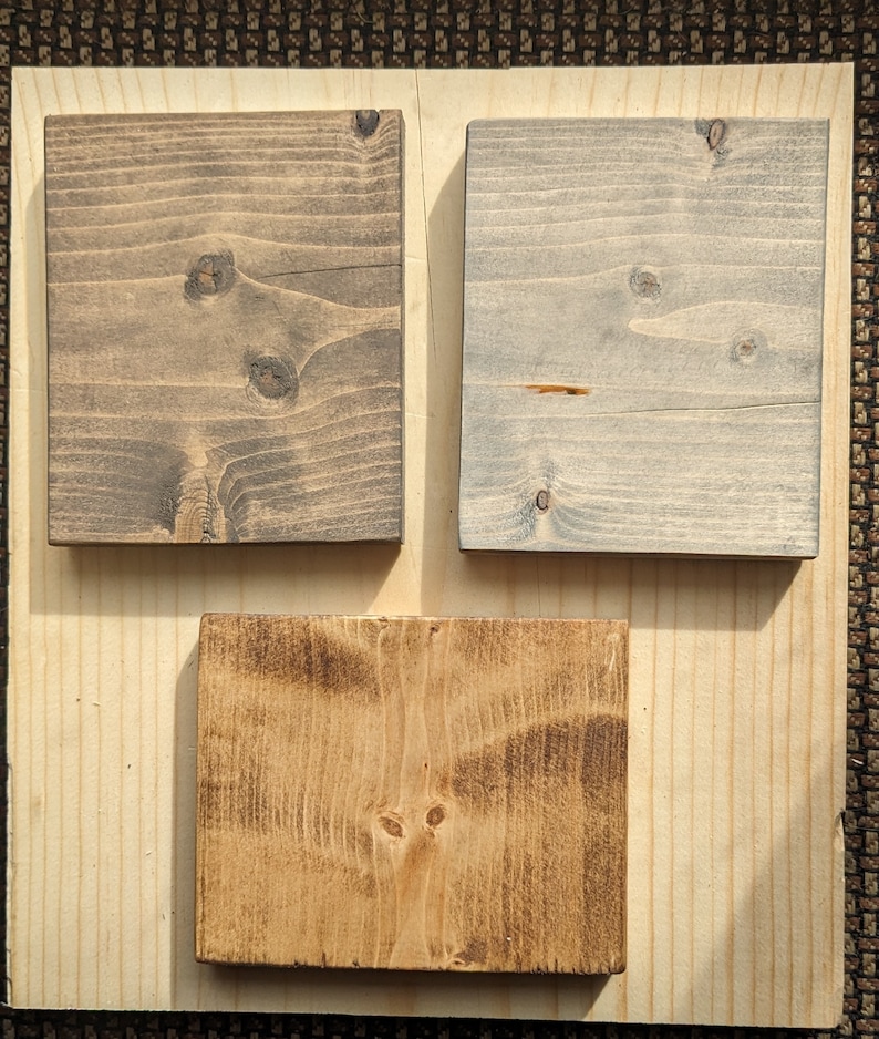 May include: Three wood samples stained in different colors. The first sample is a dark brown color, the second sample is a light gray color, and the third sample is a medium brown color.