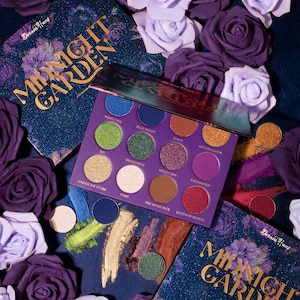 Może przedstawiać: Fioletowa paleta cieni do powiek z napisem "MIDNIGHT GARDEN" i różnymi kolorami cieni, w tym niebieskim, zielonym, złotym i fioletowym. Paleta otoczona jest fioletowymi i lawendowymi różami.